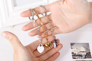 Detailed view of three stainless steel keychains with heart and figure charms in hand