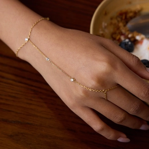 Golden stainless steel finger chain bracelet with white cubic zirconia on a female hand