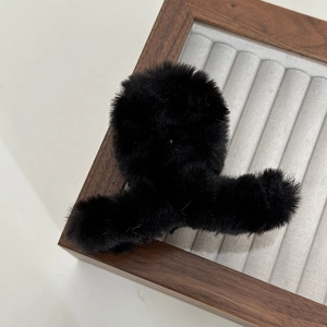 Detail view of a black faux fur hair claw clip on a wooden display tray with soft texture