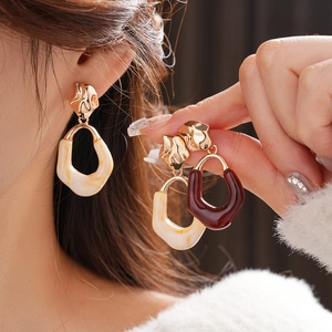 Macro detail of oval resin earrings in cream marble and dark burgundy with gold metal