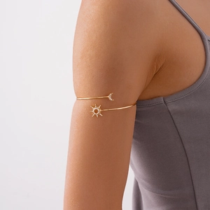 Detail shot of a golden sun and moon arm cuff inlaid with zircon on a model's upper arm