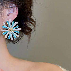 Vista dettagliata dell'orecchino a fiore in smalto blu e bianco indossato da una modella
