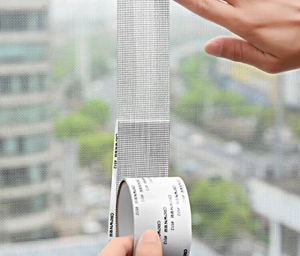 Close-up of grey mesh screen repair tape being applied to a window with self-adhesive backing
