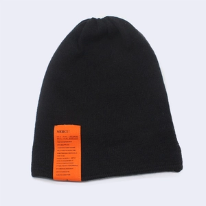Detailed close-up of a black knit beanie with a bright orange woven label and fine texture