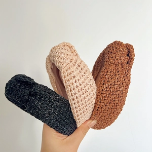 Détail de serre-têtes en paille tressée noire, beige et marron tenus à la main