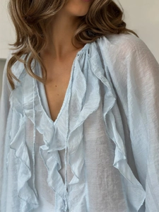 Close-up of light blue V-neck blouse with tiered ruffles and sheer textured fabric