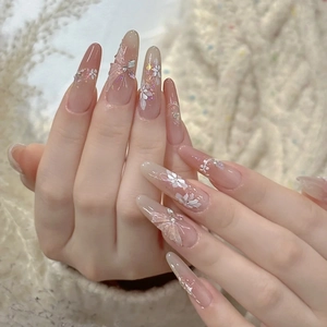 Long almond press-on nails with nude pink gradient, white flowers and 3D bows decoration
