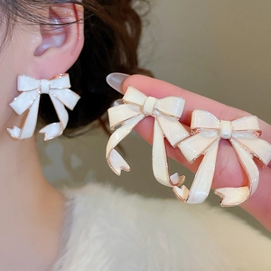 Close-up of elegant white ribbon bow earrings with gold plating and enamel finish