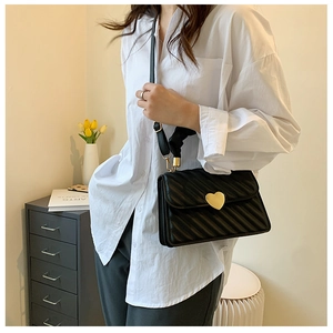 Detail of black quilted crossbody bag featuring a gold heart clasp and accordion folds