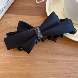 Detail of elegant black satin bow hair clip with sparkling crystal inlay on a wooden desk