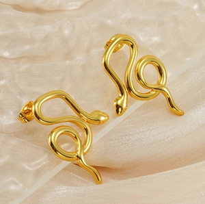 Vue détaillée de boucles d'oreilles serpent dorées sur tissu beige texturé