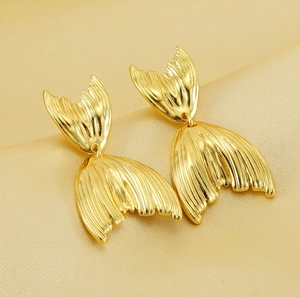 Macro shot of gold-plated fishtail earrings on silk fabric with textured fin details