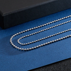 Macro detail of silver stainless steel ball bead necklace chains on a textured dark background