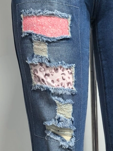Dettaglio dei jeans blu con toppe rosa testurizzate e stampa leopardata consumata