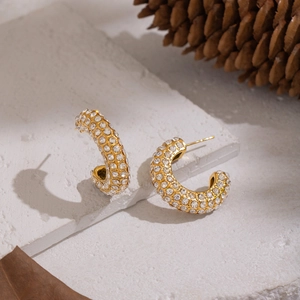 Gros plan de boucles d'oreilles créoles dorées en C avec strass sur des pierres naturelles