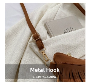 Detail view of gold hardware hooks and tassels on a brown suede crossbody bag