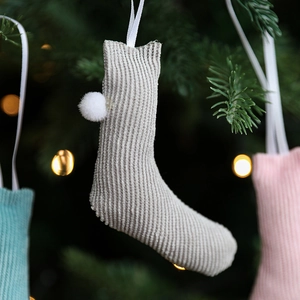 Knitted grey-beige Christmas stocking with pom-pom hanging on a festive decorated pine tree