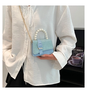 Detail of light blue crossbody bag with pearl handle and glitter woven fabric finish