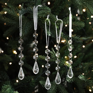 Set of clear acrylic snowflake ornaments hanging on a Christmas tree with festive lights