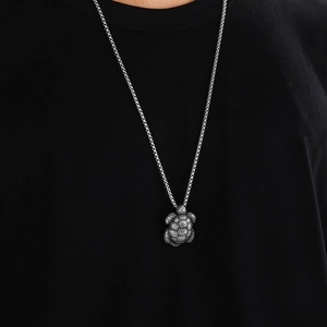 Close-up of a vintage silver turtle pendant with intricate textures on a black t-shirt
