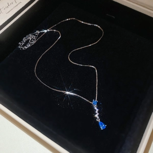 Detailed view of silver box chain with square and teardrop blue zircon pendants on black velvet