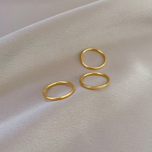 Detailed view of three minimalist gold titanium rings on a soft silk background