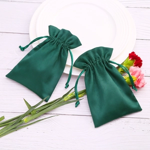 Detailed view of dark green drawstring velvet jewelry bags on a white textured background