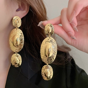 Exaggerated golden oval geometric tassel earrings with hammered texture on a model