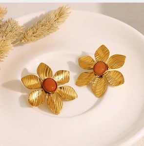 Detailed macro view of gold flower earrings with orange stones on a ceramic tray