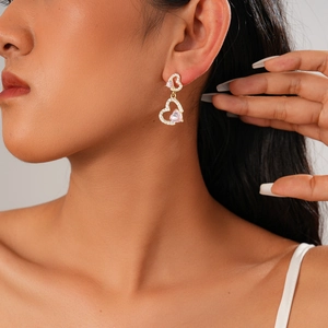 Close-up of golden heart earrings with pink gems and rhinestones on female model