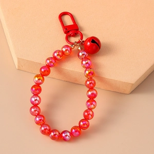 Close-up of a red beaded keychain with a metal bell on a beige geometric block