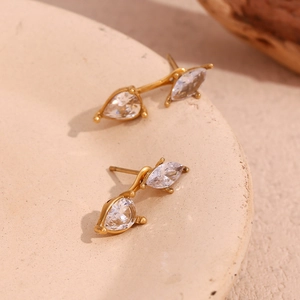 Macro shot of 18K gold-plated teardrop zircon earrings on a beige textured ceramic plate