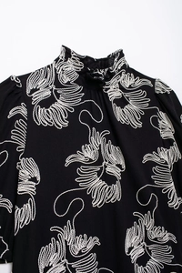Close-up of white floral embroidery on a black mock neck short sleeve blouse