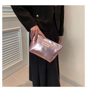 Detail of rose gold metallic clutch with fashion bag label held by a person in a suit