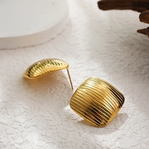 Macro shot of 18k gold plated square earrings with unique striped texture on wood surface