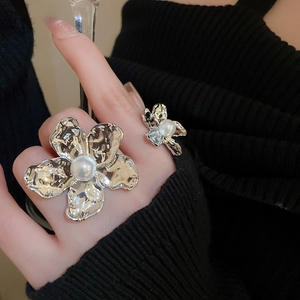 Detailed close-up of irregular silver floral rings with pearls on dark knit background