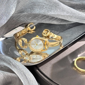 Detail showing vintage golden horseshoe-style watch case with silver dial on reflective tray