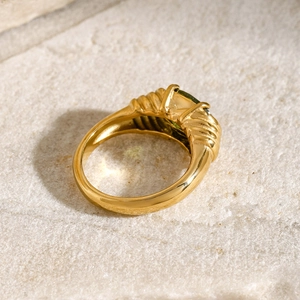 Detail of 18k gold plated ring with wave texture and emerald-cut green gemstone