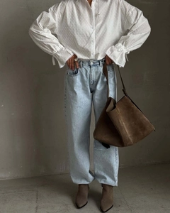Detail of white textured polka dot blouse paired with blue jeans and brown suede bag