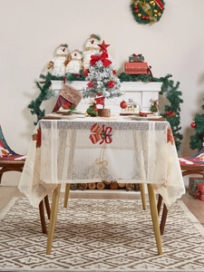 Detailed embroidery of festive bells and red bows on a beige lace Christmas tablecloth