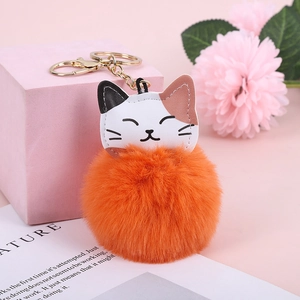 Detail of cute calico cat leather head with large orange faux fur pompom and gold keychain