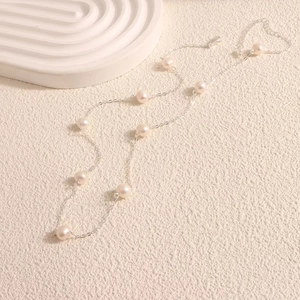 Macro shot of minimalist silver necklace featuring uniform freshwater pearls on a delicate chain