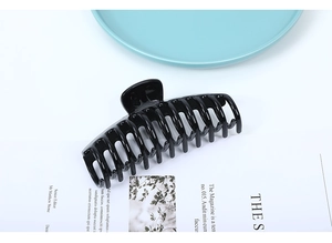 Close-up of a large glossy black shark hair claw clip placed on a stylish magazine