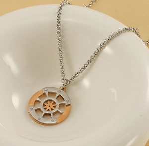 Macro shot of two-tone stainless steel nautical compass pendant in a white ceramic bowl