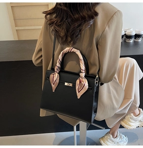 Détail d'un sac à main noir structuré avec un foulard en soie rayé enroulé autour de l'anse