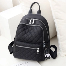 Detail of black quilted backpack with silver zippers and a cute bear keychain accessory