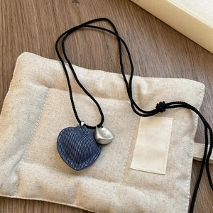 Detail of dark blue denim heart pendant with silver charm on black woven cord necklace