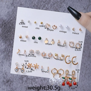 Detail of diverse earrings set featuring gold finish pearls and cherry pendants on cards