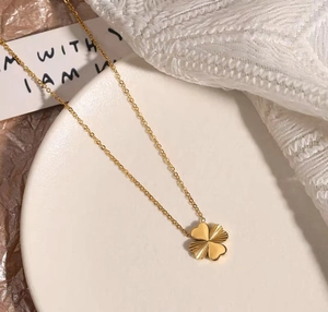 Detailed view of a gold four-leaf clover pendant necklace on a decorative white plate