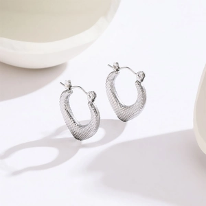 Close-up of silver textured heart earrings with grainy pattern and secure clasp
